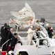 Pope Frances driving through Vatican City with the carcass of his six-winged seraph splayed out and strapped down across the Popemobile’s roof.